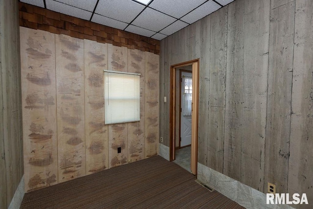 unfurnished room featuring carpet, a drop ceiling, and wood walls