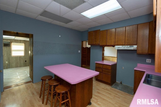 kitchen with a paneled ceiling, a kitchen breakfast bar, and light wood-type flooring