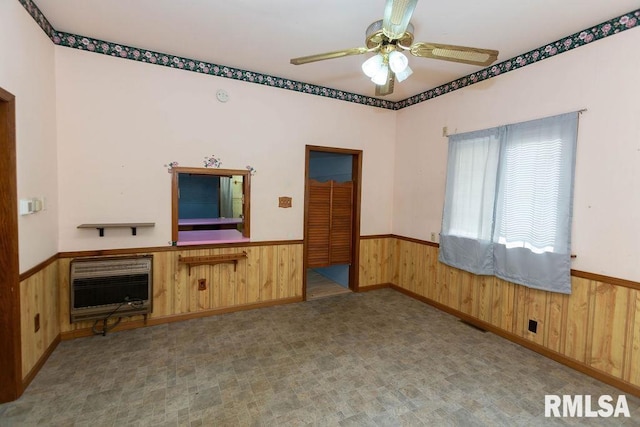 unfurnished living room with heating unit, ceiling fan, and wood walls