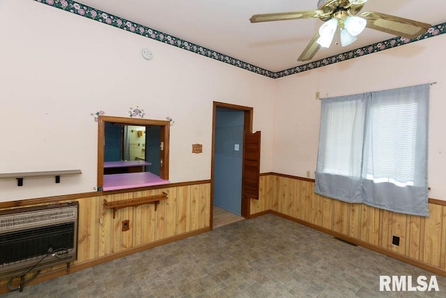 interior space featuring ceiling fan, wooden walls, and heating unit