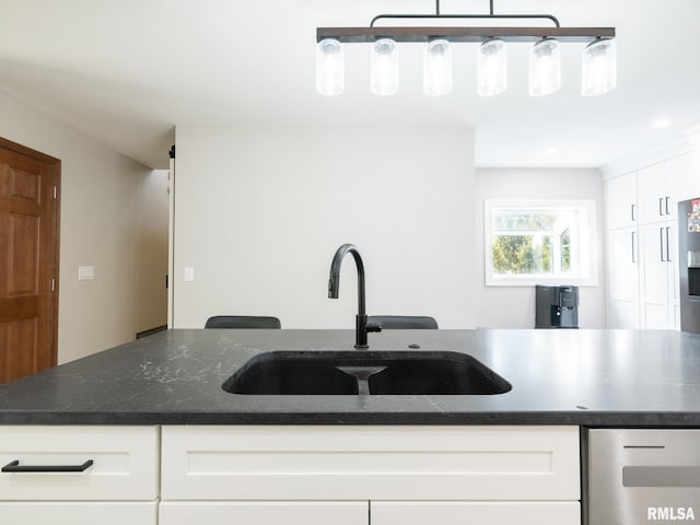 kitchen with white cabinetry, dishwasher, sink, dark stone countertops, and hanging light fixtures