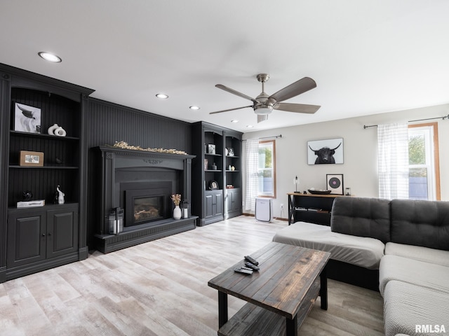 living room with built in shelves, ceiling fan, and light wood-type flooring