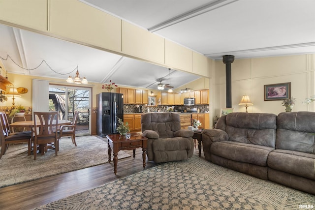 living room featuring hardwood / wood-style floors, ceiling fan with notable chandelier, vaulted ceiling, and a wood stove