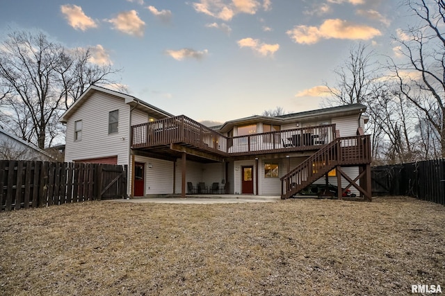 back house at dusk featuring a wooden deck, a yard, and a patio area