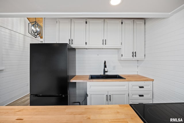 kitchen featuring cooktop, sink, butcher block countertops, black fridge, and decorative light fixtures