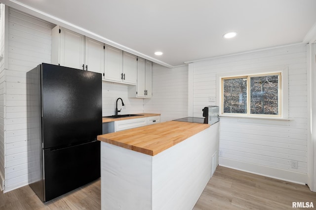 kitchen with light wood-type flooring, butcher block counters, sink, and black appliances