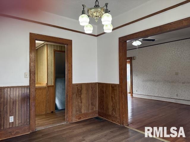 unfurnished dining area with crown molding, dark hardwood / wood-style floors, a chandelier, and wood walls