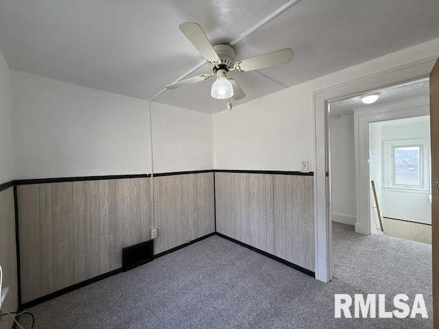 carpeted spare room featuring wooden walls and ceiling fan