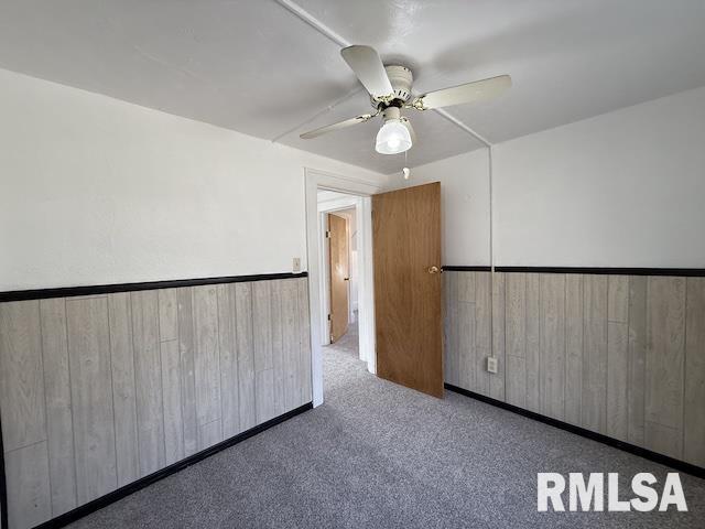 carpeted spare room with ceiling fan and wood walls