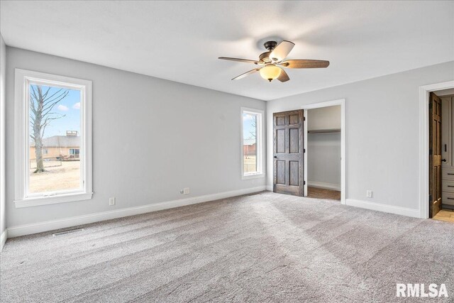 unfurnished bedroom with a spacious closet, light colored carpet, ceiling fan, and ensuite bathroom