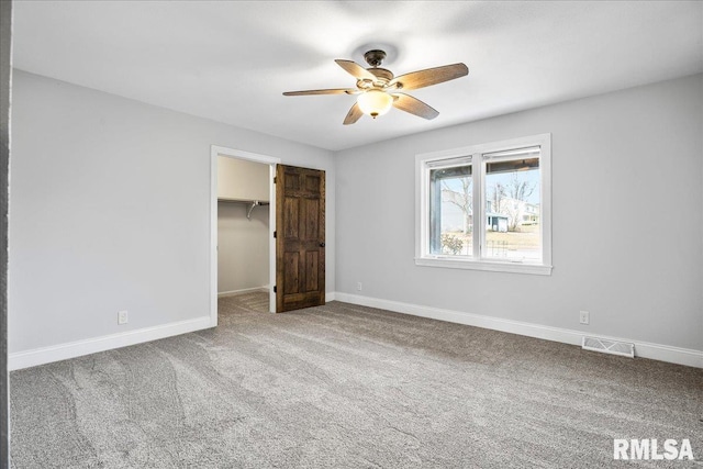 unfurnished bedroom featuring a closet, carpet flooring, ceiling fan, and a spacious closet