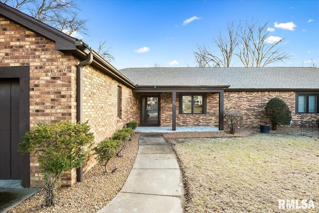 view of exterior entry featuring a shingled roof, a lawn, and brick siding