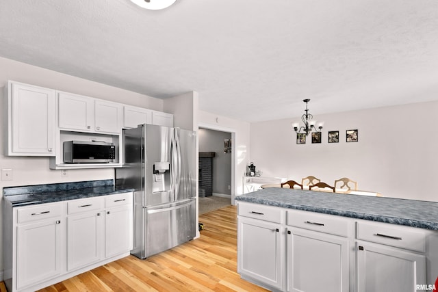 kitchen with appliances with stainless steel finishes, decorative light fixtures, white cabinets, a notable chandelier, and light hardwood / wood-style flooring