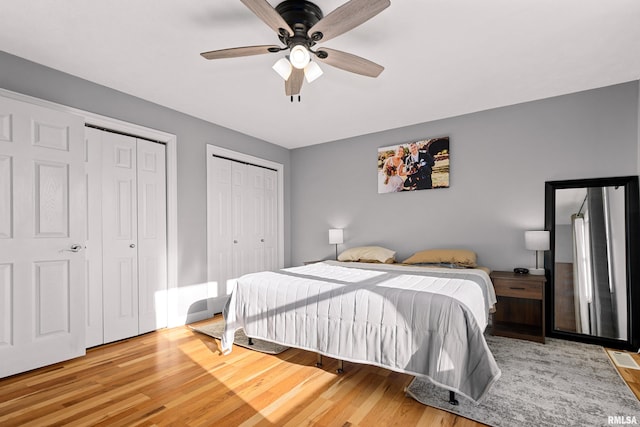 bedroom featuring multiple closets, hardwood / wood-style flooring, and ceiling fan