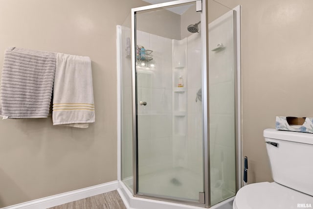 bathroom with hardwood / wood-style flooring, a shower with door, and toilet