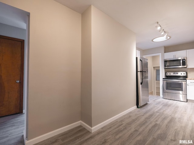 kitchen featuring appliances with stainless steel finishes, white cabinets, track lighting, hardwood / wood-style flooring, and decorative backsplash