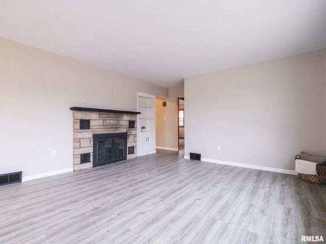 unfurnished living room featuring a stone fireplace and light wood-type flooring