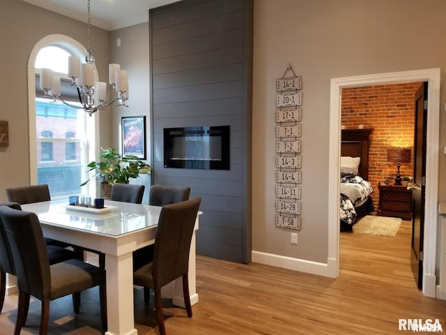 dining area with a notable chandelier, ornamental molding, light hardwood / wood-style floors, and a fireplace