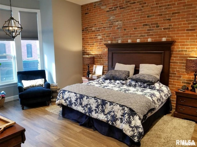 bedroom featuring brick wall, hardwood / wood-style floors, and a chandelier