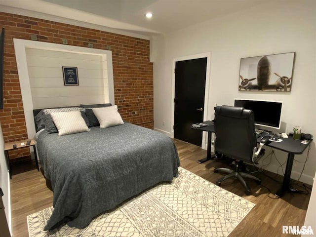 bedroom featuring brick wall and hardwood / wood-style floors