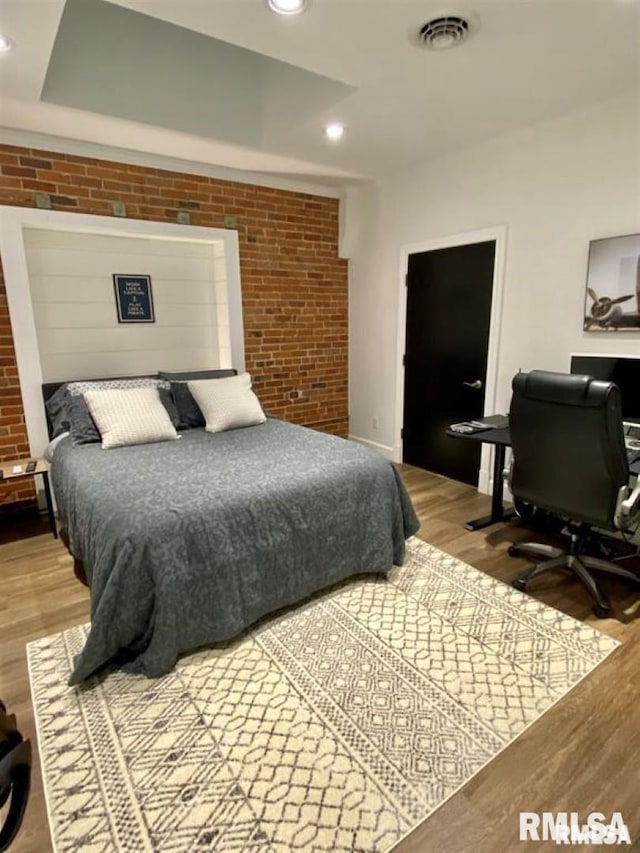 bedroom with brick wall and hardwood / wood-style floors