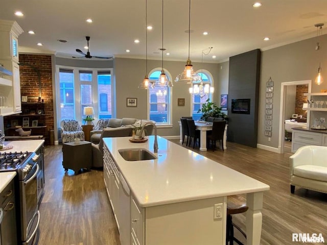 kitchen with white cabinetry, a center island with sink, stainless steel gas range, and decorative light fixtures