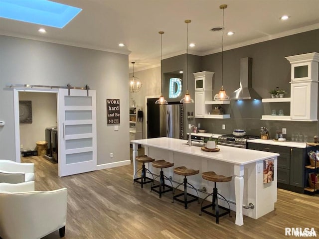 kitchen with extractor fan, pendant lighting, stainless steel appliances, a barn door, and a kitchen island with sink