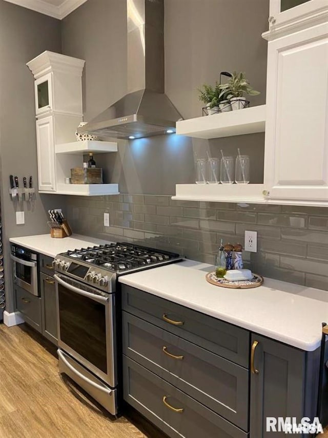 kitchen featuring light hardwood / wood-style flooring, appliances with stainless steel finishes, white cabinetry, backsplash, and wall chimney exhaust hood