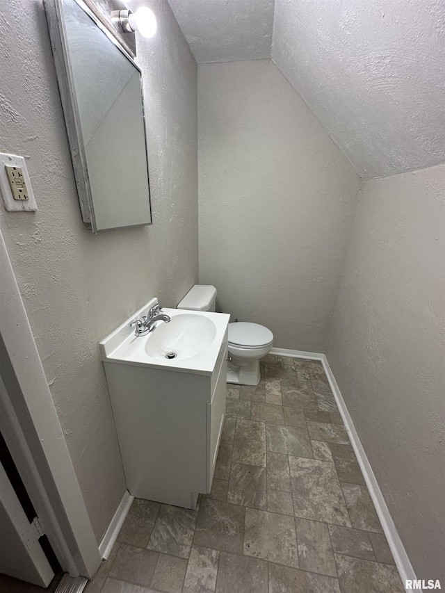 bathroom featuring vanity, vaulted ceiling, a textured ceiling, and toilet