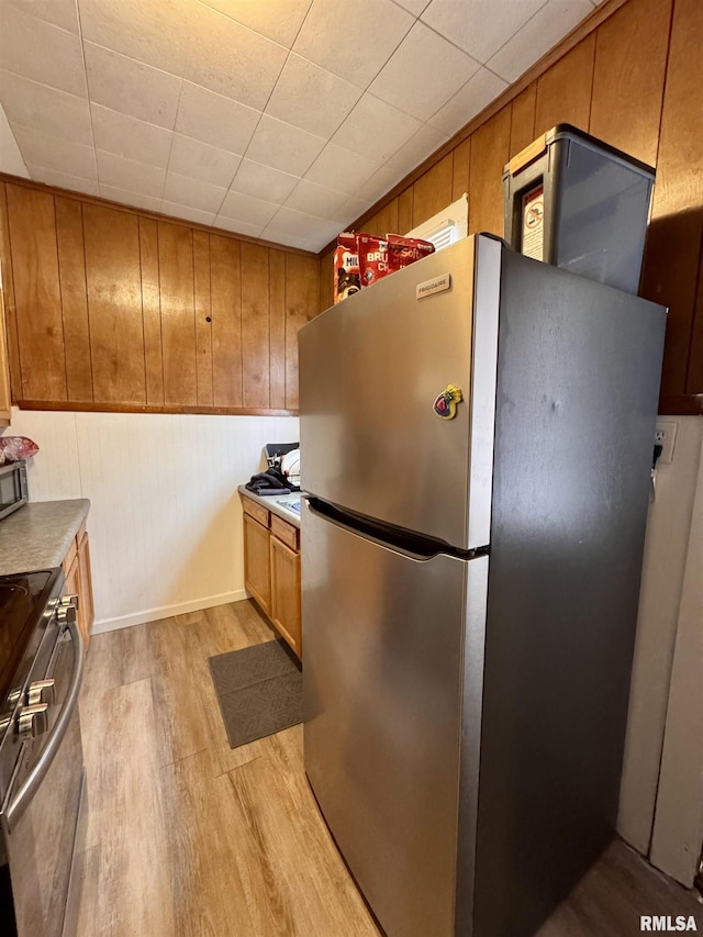 kitchen with appliances with stainless steel finishes, wooden walls, and light hardwood / wood-style flooring