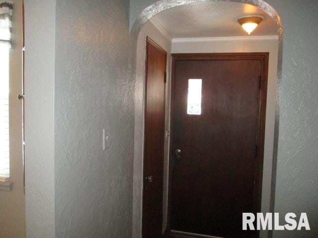 entryway featuring arched walkways, crown molding, and a textured wall