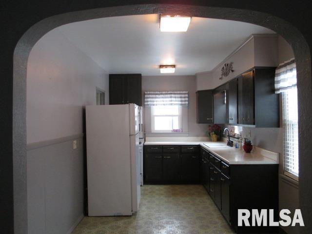 kitchen with arched walkways, light floors, light countertops, freestanding refrigerator, and a sink