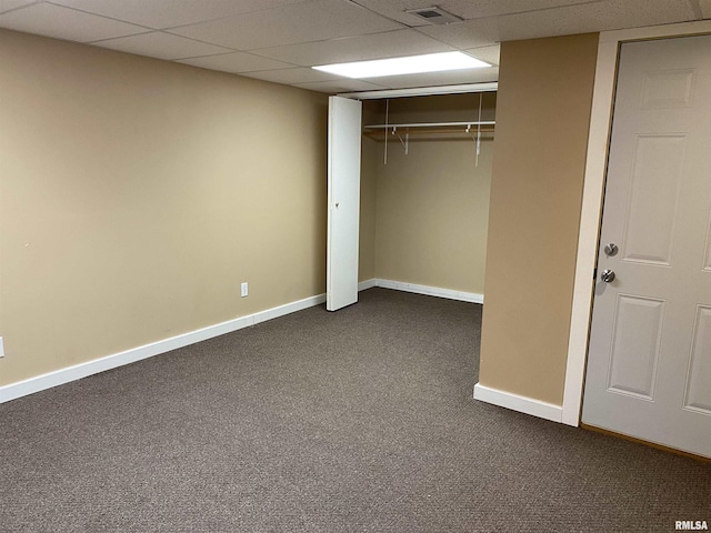 unfurnished bedroom with a paneled ceiling, dark carpet, and a closet