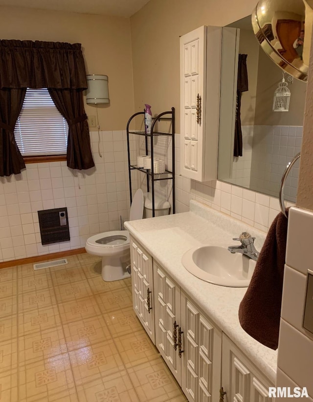 bathroom with heating unit, vanity, toilet, and tile walls