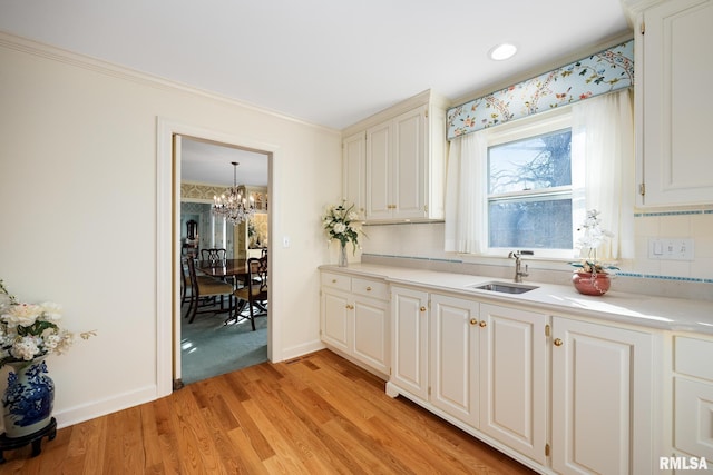 kitchen with white cabinetry, sink, backsplash, light hardwood / wood-style floors, and an inviting chandelier