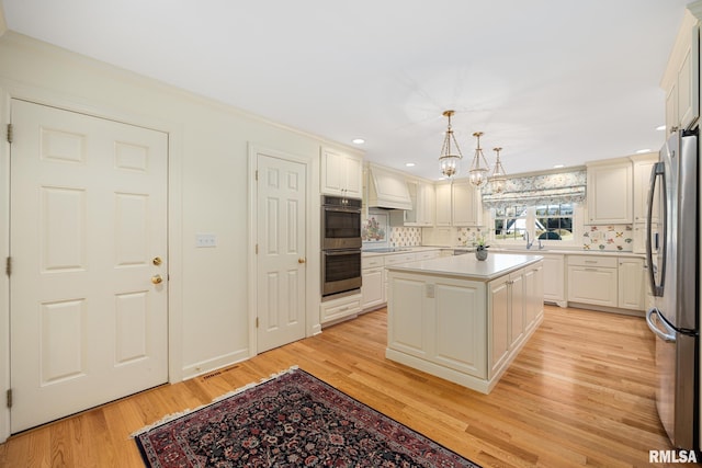 kitchen with a kitchen island, appliances with stainless steel finishes, decorative light fixtures, tasteful backsplash, and light hardwood / wood-style floors