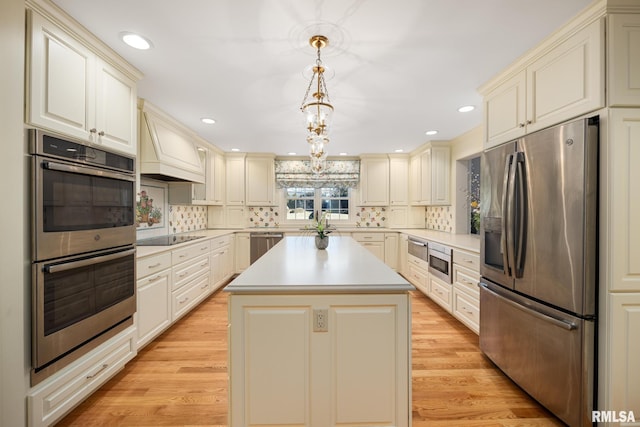 kitchen with decorative light fixtures, custom range hood, a kitchen island, stainless steel appliances, and cream cabinetry