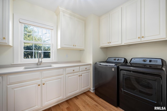 laundry room featuring washer and dryer, sink, cabinets, and light hardwood / wood-style flooring