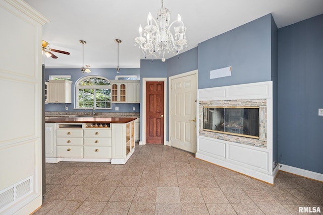 kitchen featuring sink, butcher block countertops, hanging light fixtures, a fireplace, and ceiling fan with notable chandelier