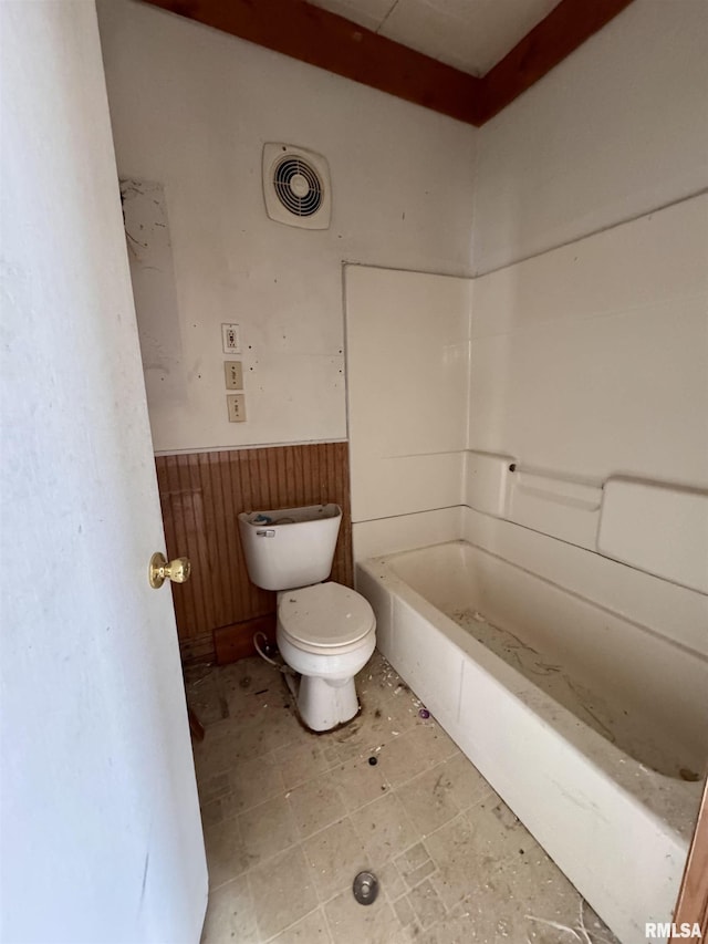 bathroom featuring a tub, wooden walls, and toilet