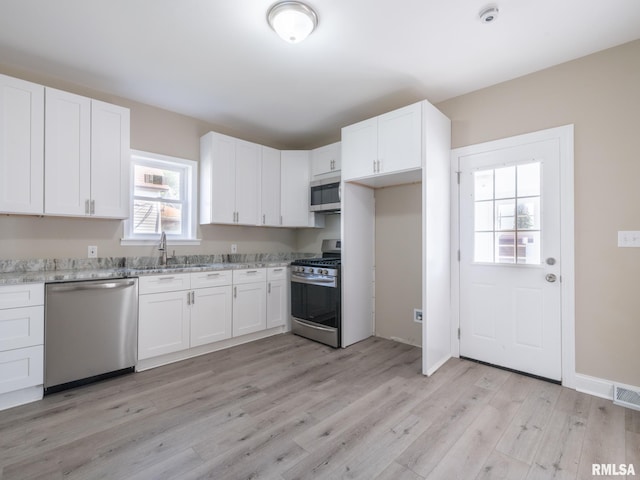 kitchen with sink, stainless steel appliances, light stone counters, white cabinets, and light wood-type flooring