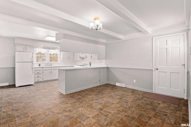 kitchen with a wainscoted wall, a peninsula, white cabinets, light countertops, and freestanding refrigerator