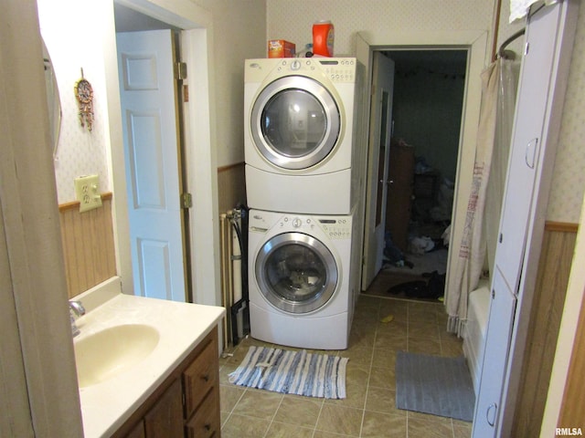 washroom with light tile patterned flooring, stacked washing maching and dryer, and sink