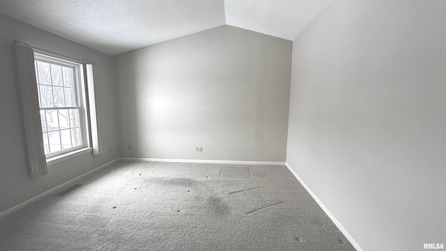 empty room with baseboards, visible vents, vaulted ceiling, a textured ceiling, and carpet floors