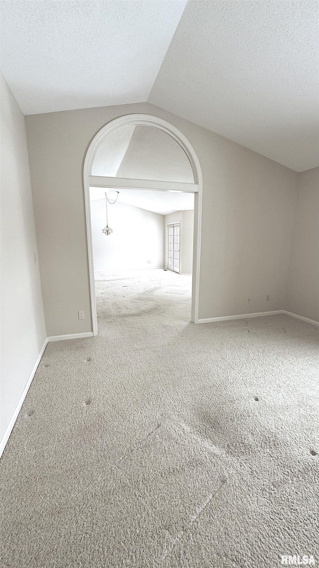 carpeted empty room with vaulted ceiling, a textured ceiling, and baseboards