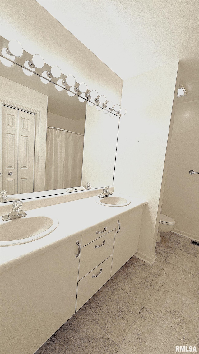 full bathroom with toilet, double vanity, baseboards, and a sink