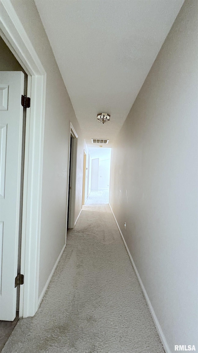 corridor featuring light carpet, visible vents, and baseboards