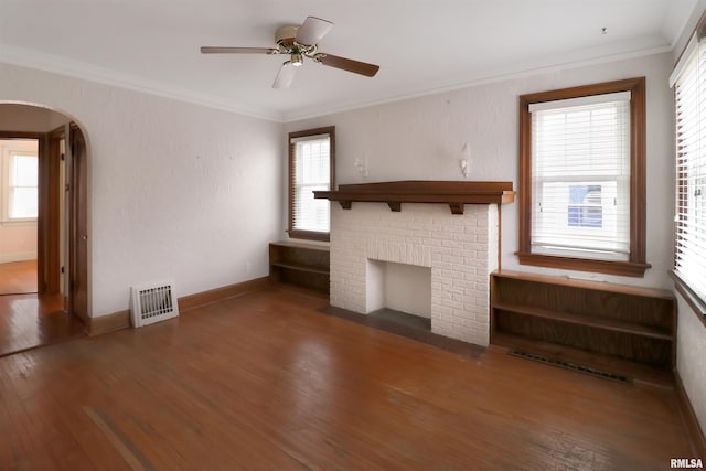 unfurnished living room featuring dark wood-type flooring, a brick fireplace, crown molding, and ceiling fan