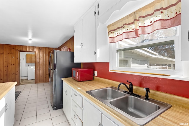 kitchen featuring light tile patterned flooring, washer / dryer, sink, wooden walls, and white cabinets