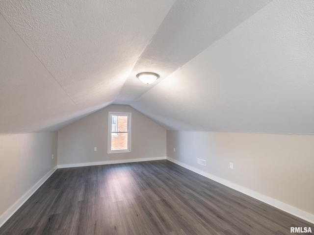 additional living space featuring dark wood-type flooring, a textured ceiling, and vaulted ceiling